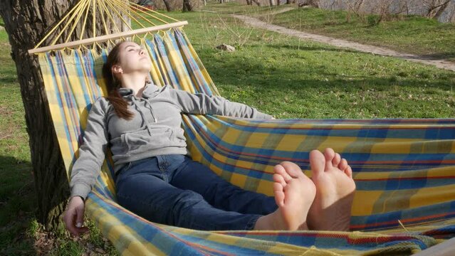A beautiful girl is resting in nature, lying in a hammock with barefoot.