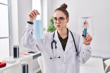 Fototapeta premium Young hispanic girl holding medical asthma inhaler at the clinic puffing cheeks with funny face. mouth inflated with air, catching air.