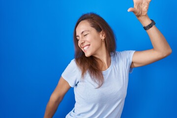 Fototapeta premium Brunette woman standing over blue background dancing happy and cheerful, smiling moving casual and confident listening to music