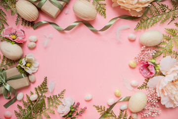Obraz na płótnie Canvas beautiful easter frame composition with wooden easter eggs, flowers, ribbons and gifts on a pastel pink background. top view. copy space. flat lay. place for text.