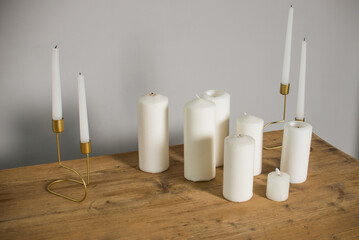 a composition of white candles of various sizes and thicknesses on a light wood countertop.
