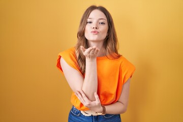 Caucasian woman standing over yellow background looking at the camera blowing a kiss with hand on air being lovely and sexy. love expression.