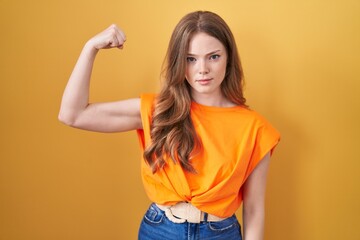 Caucasian woman standing over yellow background strong person showing arm muscle, confident and...