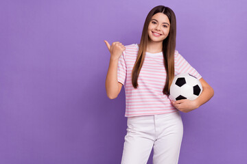 Photo of cheerful cute girl hold football direct finger empty space isolated on violet color background