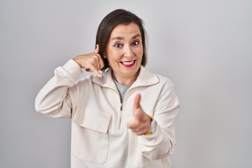 Middle age hispanic woman standing over isolated background smiling doing talking on the telephone gesture and pointing to you. call me.