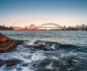 Meer und Wellen im Abendlicht mit Opernhaus und Brücke in Sydney.