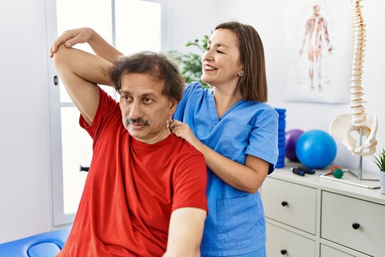 Middle age man and woman wearing physiotherapy uniform having rehab session stretching arm at physiotherapy clinic