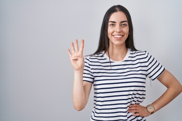 Young brunette woman wearing striped t shirt showing and pointing up with fingers number four while smiling confident and happy.