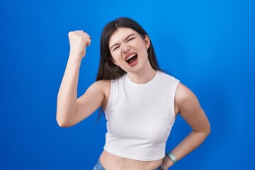 Fototapeta na wymiar Young caucasian woman standing over blue background angry and mad raising fist frustrated and furious while shouting with anger. rage and aggressive concept.