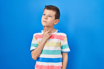 Young caucasian kid standing over blue background thinking concentrated about doubt with finger on chin and looking up wondering
