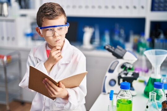 Blond child wearing scientist uniform reading book at laboratory