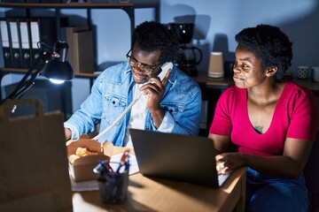African american man and woman business workers using laptop talking on the telephone at office