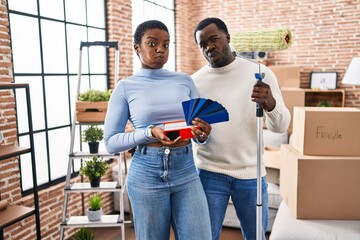 Young african american couple moving to a new home choosing walls color puffing cheeks with funny face. mouth inflated with air, catching air.