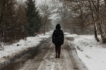 Fototapeta na wymiar walking person in black jacket on the country road on a sad snowy winter day