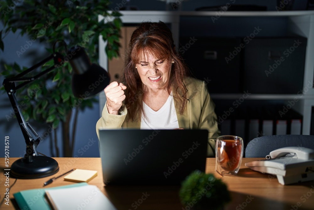 Canvas Prints middle age hispanic woman working using computer laptop at night angry and mad raising fist frustrat