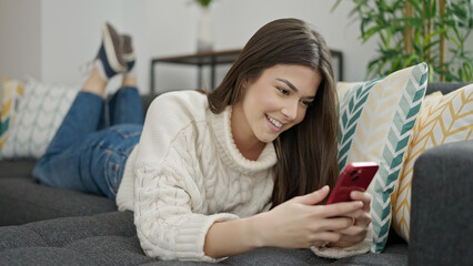 Young beautiful hispanic woman using smartphone lying on sofa at home