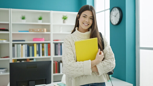 Young beautiful hispanic woman student smiling confident holding book at university classroom