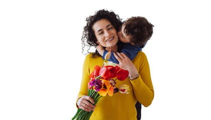 Curly hispanic little boy standing  at table hugging mom, kissing her at cheek, mother holding colourful tulips eyes closed against transparent background. Italian housewife received flowers from son.