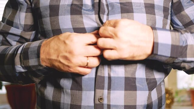 A man unbuttons the buttons on a plaid shirt one by one in turn with his hands.