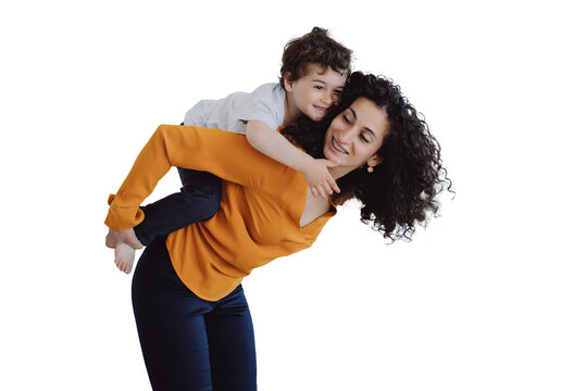 Playful curly Italian boy  riding on mom against transparent background. Hispanic woman babysitter rolling up on back cheerful kid at home. Caucasian sister entertains  brother. Childhood, maternity