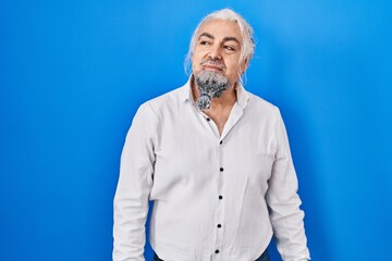 Middle age man with grey hair standing over blue background smiling looking to the side and staring away thinking.