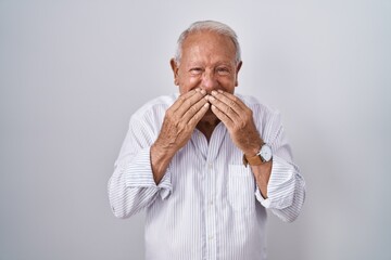 Senior man with grey hair standing over isolated background laughing and embarrassed giggle...
