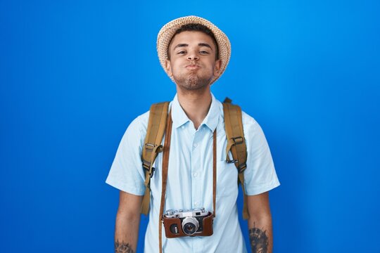 Brazilian young man holding vintage camera puffing cheeks with funny face. mouth inflated with air, crazy expression.