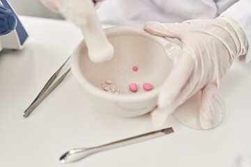 Young beautiful hispanic woman scientist crushing pills on bowl at laboratory
