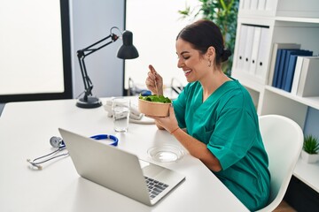 Young beautiful hispanic woman doctor smiling confident eating salad at clinic