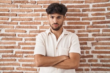 Arab man with beard standing over bricks wall background skeptic and nervous, disapproving expression on face with crossed arms. negative person.