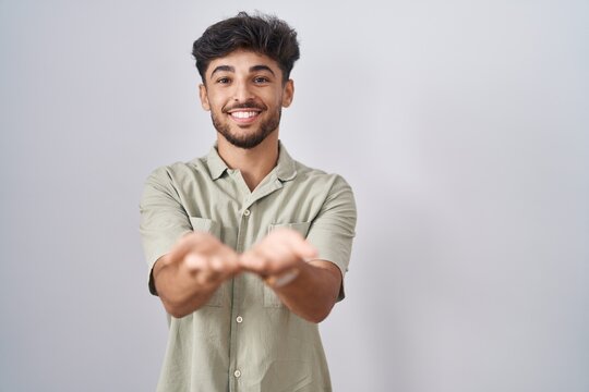 Arab man with beard standing over white background smiling with hands palms together receiving or giving gesture. hold and protection