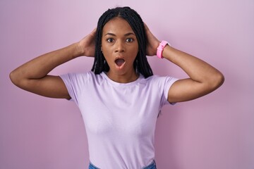 African american woman with braids standing over pink background crazy and scared with hands on head, afraid and surprised of shock with open mouth