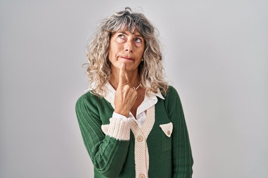 Middle age woman standing over white background thinking concentrated about doubt with finger on chin and looking up wondering