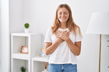 Young blonde girl standing with hands on heart at home