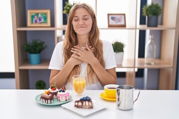 Obraz na płótnie Canvas Young caucasian woman eating pastries t for breakfast smiling with hands on chest with closed eyes and grateful gesture on face. health concept.