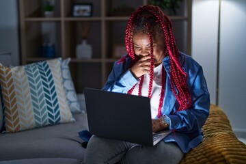 African american woman with braided hair using computer laptop at night laughing and embarrassed...