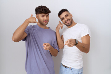 Homosexual gay couple standing over white background smiling doing talking on the telephone gesture...