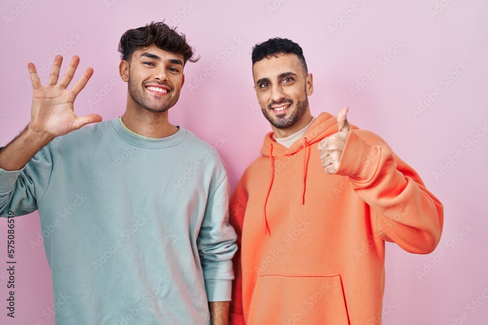 Poster young hispanic gay couple standing over pink background showing and pointing up with fingers number 