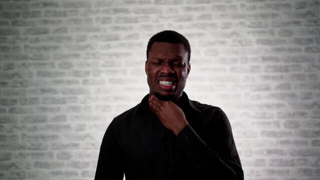 Portrait of stressed handsome African american man with throat pain isolated on brick wall background.