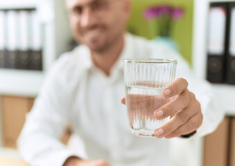 Young hispanic man business worker holding glass of water at office