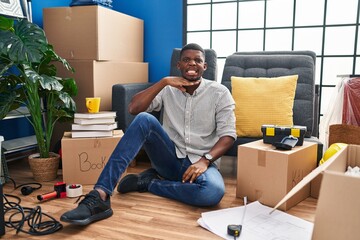 African american man sitting on the floor at new home cutting throat with hand as knife, threaten aggression with furious violence