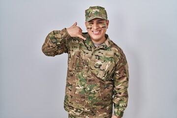 Hispanic young man wearing camouflage army uniform smiling doing phone gesture with hand and fingers like talking on the telephone. communicating concepts.