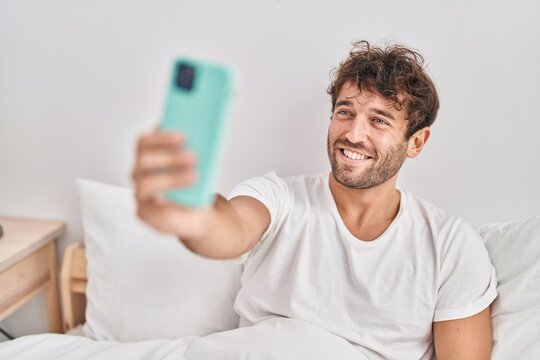 Young man make selfie by smartphone sitting on bed at bedroom