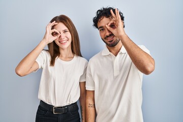 Young couple wearing casual clothes standing together doing ok gesture with hand smiling, eye looking through fingers with happy face.