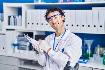 Young hispanic man scientist writing on document at laboratory