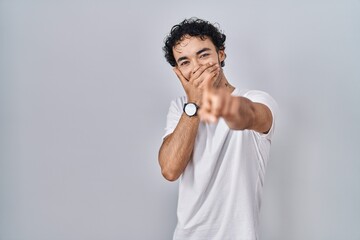 Hispanic man standing over isolated background laughing at you, pointing finger to the camera with...