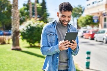Fototapeta premium Young hispanic man smiling confident using touchpad at park