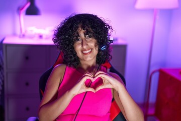 Young middle eastern woman streamer smiling confident doing heart symbol with hands at gaming room