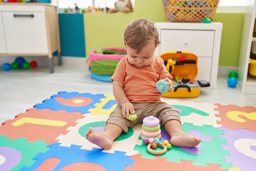 Adorable blond toddler playing with hoops toy sitting on floor at kindergarten