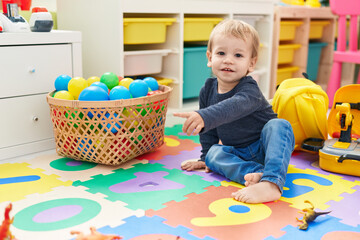 Adorable blond toddler sitting on floor pointing with finger at kindergarten